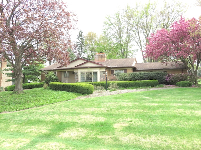 ranch-style house with a chimney, a front yard, and stone siding