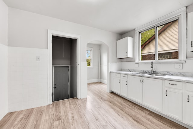 9171 Bishop St, Detroit, MI 48224 - kitchen featuring a sink, arched walkways, white cabinetry, and light wood-style flooring