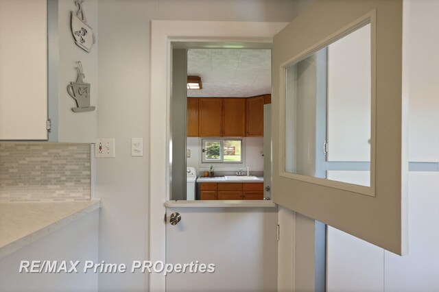kitchen with tasteful backsplash, light countertops, a sink, brown cabinets, and washer / dryer