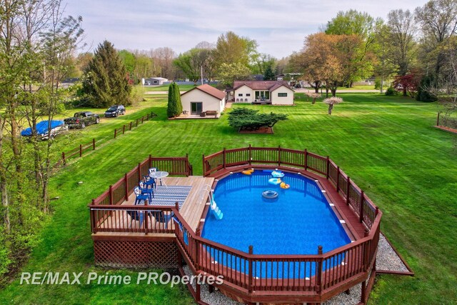 view of swimming pool featuring a wooden deck, a lawn, view of wooded area, and outdoor dining space