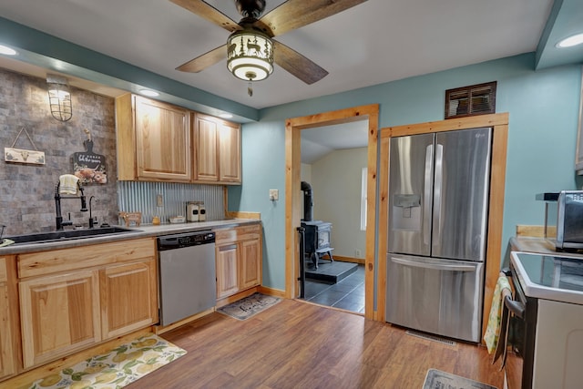 kitchen featuring stainless steel appliances, a wood stove, a sink, ceiling fan, and backsplash