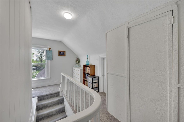 stairway featuring carpet, vaulted ceiling, and a textured ceiling