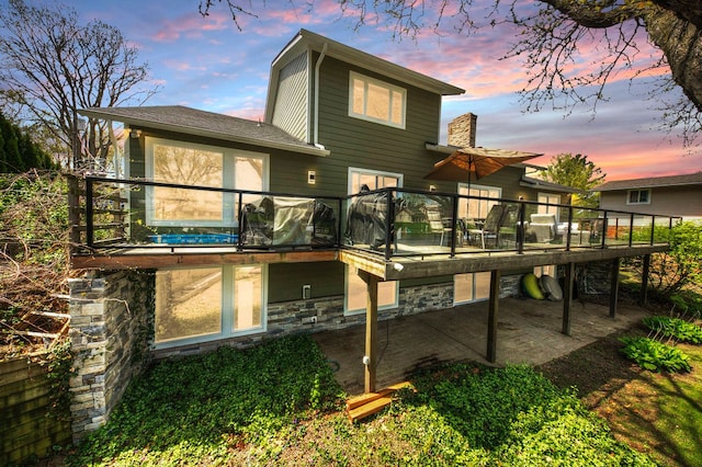 back of property with stone siding, a patio area, a wooden deck, and a chimney