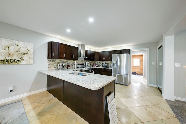 kitchen featuring appliances with stainless steel finishes, wall chimney range hood, a sink, dark brown cabinetry, and a peninsula