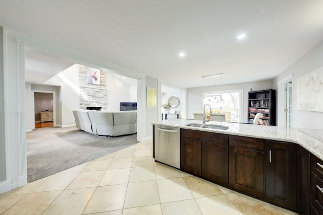 kitchen featuring a sink, dishwasher, light carpet, a fireplace, and light stone counters