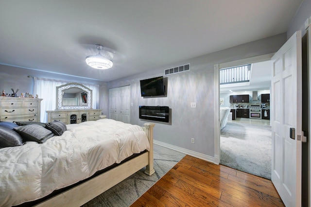 bedroom with wood-type flooring, baseboards, a closet, and a glass covered fireplace