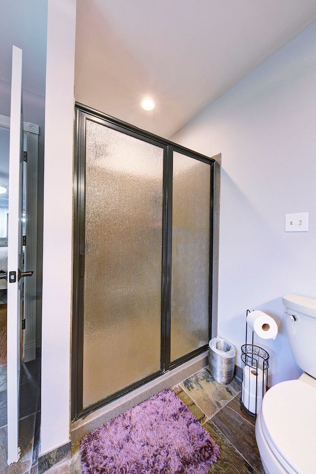 ensuite bathroom with toilet, a stall shower, and baseboards