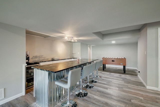 kitchen with light wood finished floors, a kitchen bar, baseboards, and a center island with sink