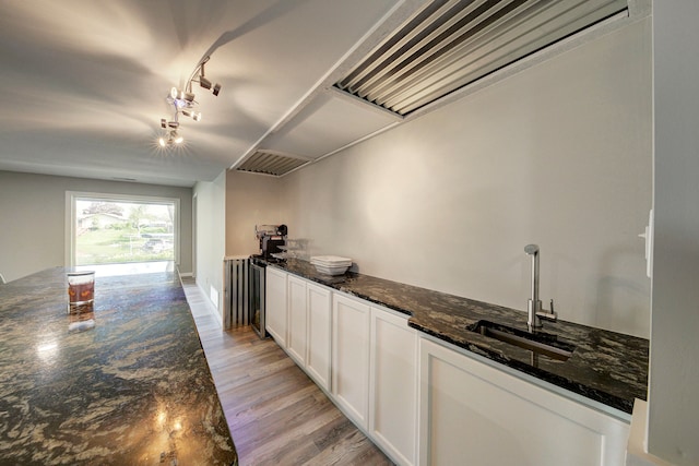 kitchen featuring a sink, rail lighting, light wood-style floors, white cabinets, and dark stone counters