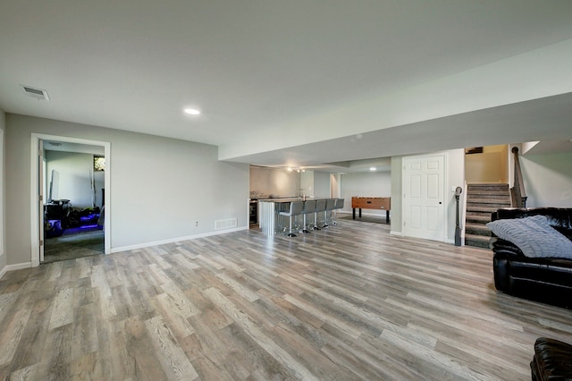 living area featuring stairs, light wood-type flooring, baseboards, recessed lighting, and bar area
