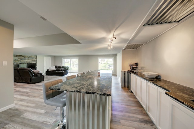 kitchen featuring light wood-style flooring, dark stone countertops, white cabinetry, and open floor plan