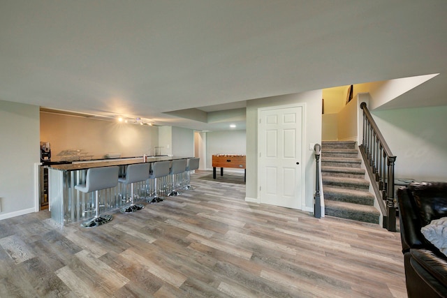 living room featuring bar, light wood-style floors, stairs, and baseboards