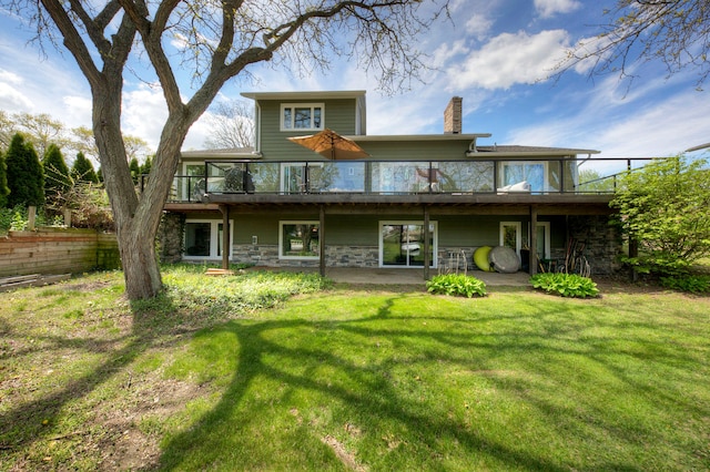 rear view of property with a chimney, a yard, stone siding, and a wooden deck