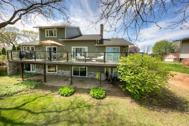 rear view of house featuring a patio area, a chimney, a deck, a yard, and stone siding