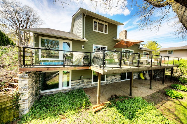 back of property with a wooden deck, stone siding, and a patio area