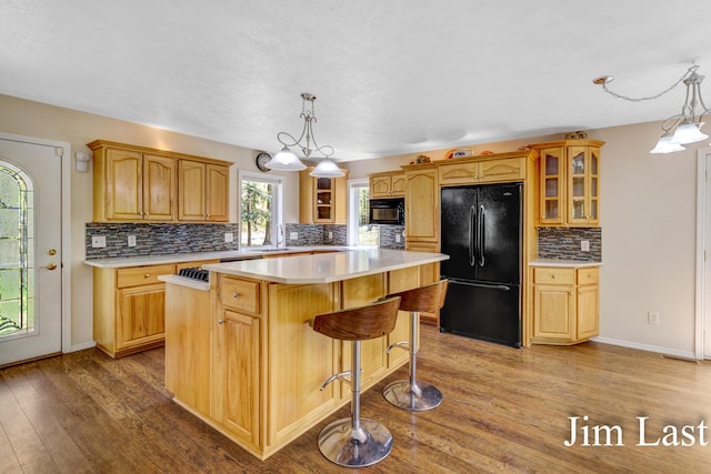 kitchen featuring black appliances, wood finished floors, a center island, glass insert cabinets, and decorative backsplash