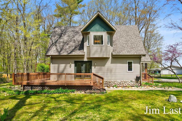 back of house featuring roof with shingles, a deck, and a lawn