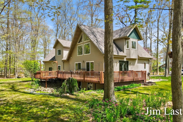 rear view of house featuring roof with shingles, a deck, and a yard