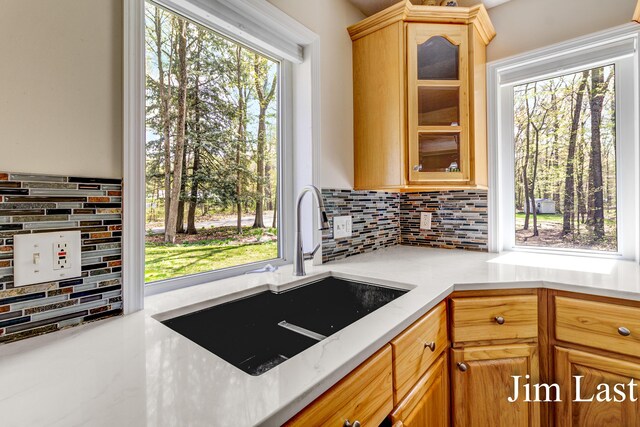 kitchen featuring a sink, decorative backsplash, glass insert cabinets, and light stone counters