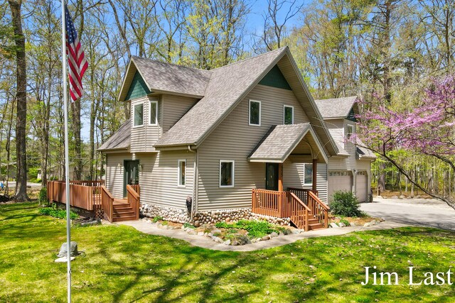 view of front of property featuring a shingled roof, driveway, a front yard, an attached garage, and a wooden deck