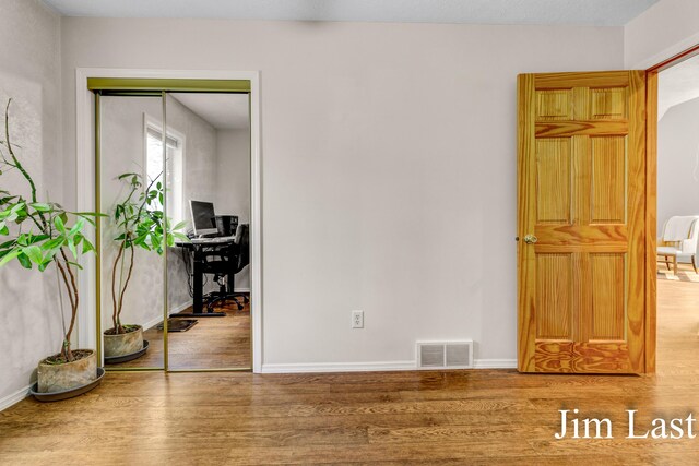 unfurnished bedroom with wood finished floors, a desk, a closet, and baseboards