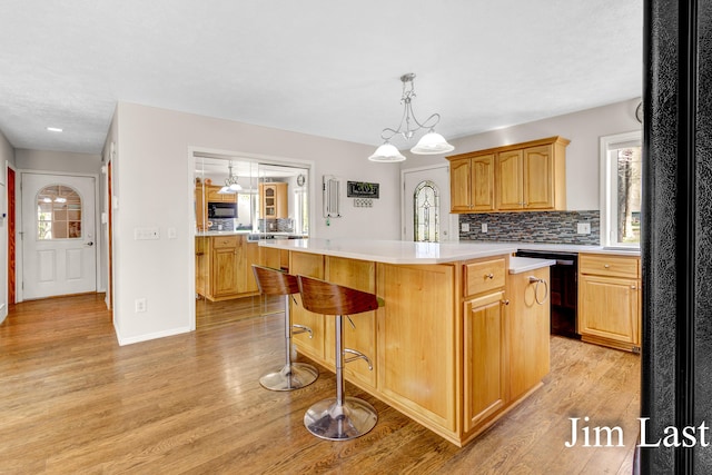 kitchen featuring black appliances, light countertops, light wood-type flooring, a center island, and decorative backsplash