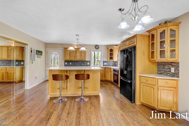 kitchen featuring black appliances, tasteful backsplash, light wood finished floors, a kitchen island, and light countertops