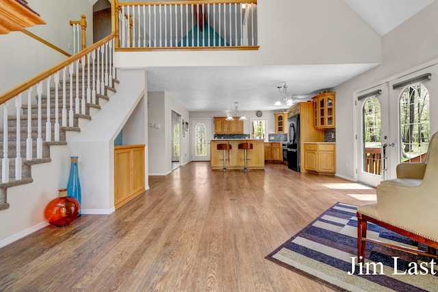 living area with french doors, light wood-style flooring, high vaulted ceiling, baseboards, and stairway