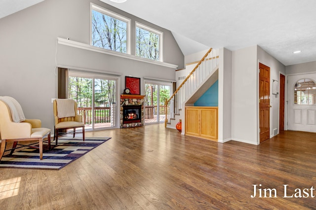 sitting room featuring wood finished floors, stairway, a stone fireplace, high vaulted ceiling, and baseboards