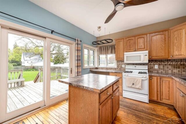 2152 6th St, Bay City, MI 48706 - kitchen with white appliances, a kitchen island, wood finished floors, decorative backsplash, and a ceiling fan