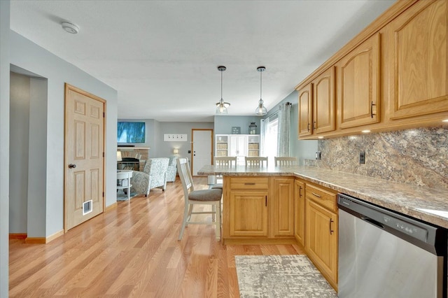 kitchen with dishwasher, light wood-type flooring, a stone fireplace, decorative backsplash, and a peninsula