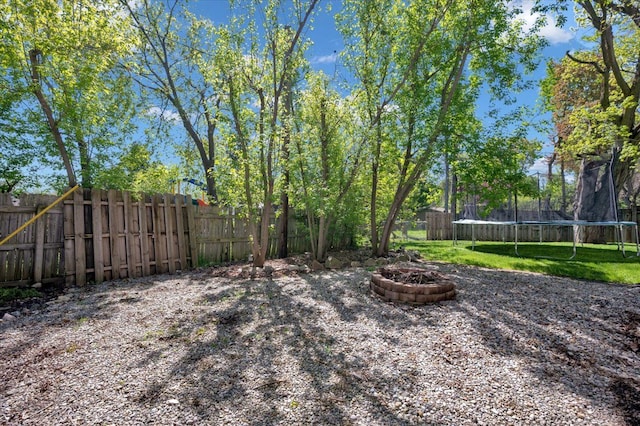 view of yard featuring a trampoline and an outdoor fire pit