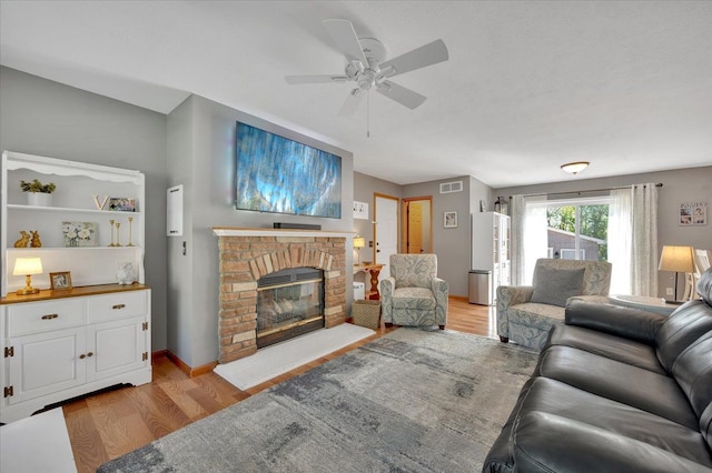 living room with light wood-type flooring, ceiling fan, a brick fireplace, and baseboards