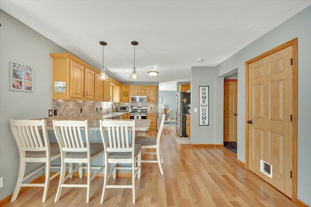 kitchen featuring appliances with stainless steel finishes, a peninsula, light countertops, tasteful backsplash, and light wood-style flooring