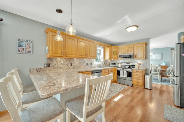 kitchen with stainless steel appliances, a peninsula, tasteful backsplash, and light wood-style floors