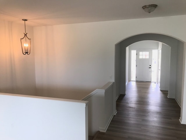 hallway with arched walkways, dark wood finished floors, and baseboards