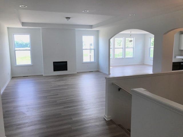 unfurnished living room with plenty of natural light, a raised ceiling, wood finished floors, and recessed lighting