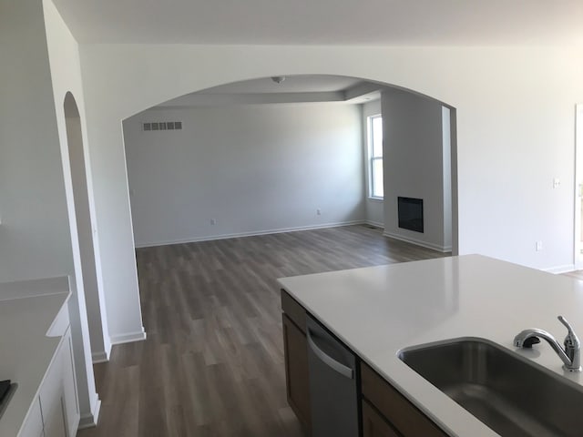 kitchen with a sink, dishwasher, dark wood-style floors, arched walkways, and light countertops
