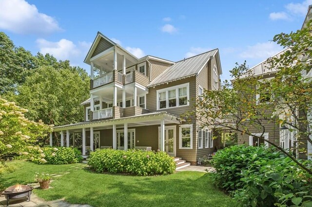 back of property featuring a fire pit, a balcony, a yard, and metal roof