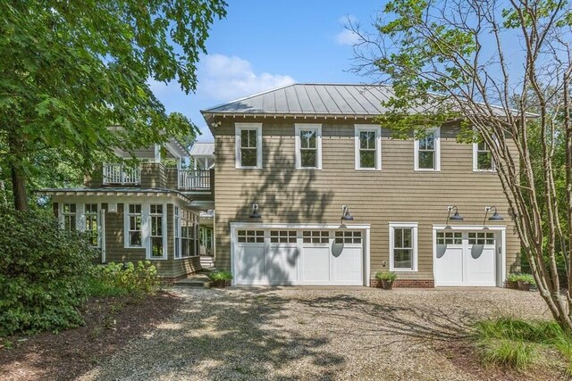 view of front of property with a garage, a standing seam roof, driveway, a balcony, and metal roof