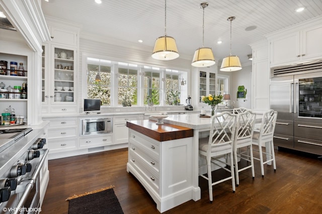 kitchen featuring built in appliances, a breakfast bar area, dark wood finished floors, wood counters, and glass insert cabinets