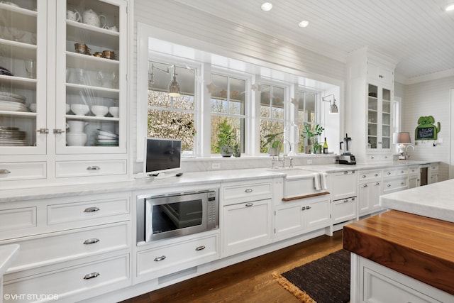 kitchen with stainless steel microwave, a sink, dark wood-style flooring, white cabinets, and glass insert cabinets
