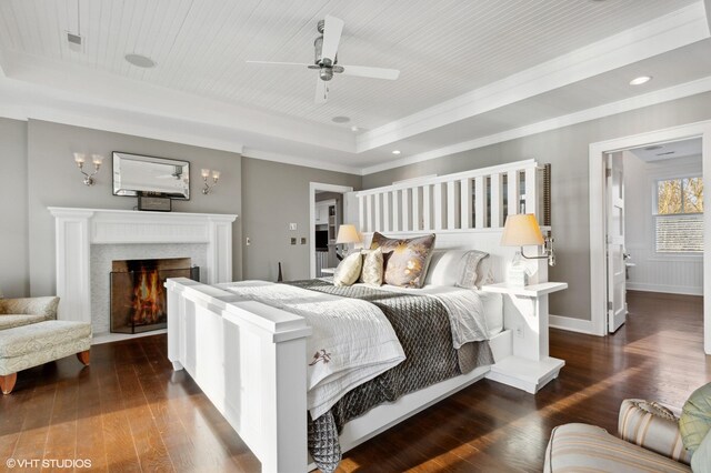 bedroom featuring a raised ceiling, ornamental molding, dark wood finished floors, baseboards, and a fireplace with flush hearth