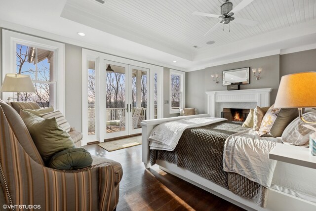 bedroom with a raised ceiling, access to outside, french doors, wood finished floors, and a lit fireplace