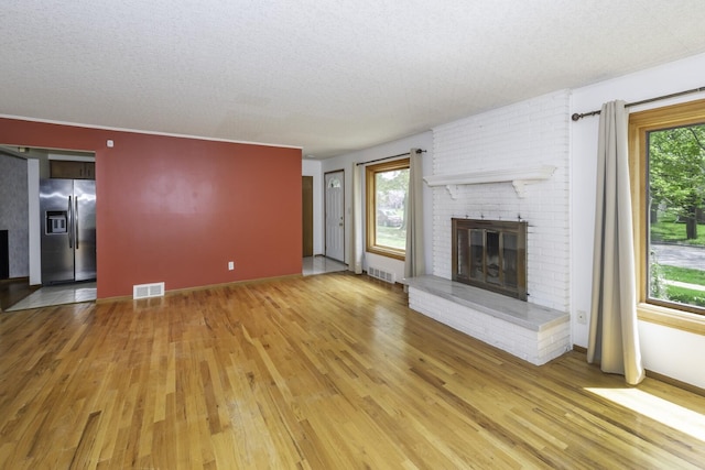 1620 Whittier Rd, Ypsilanti, MI 48197 - unfurnished living room featuring a brick fireplace, light wood finished floors, baseboards, and a textured ceiling
