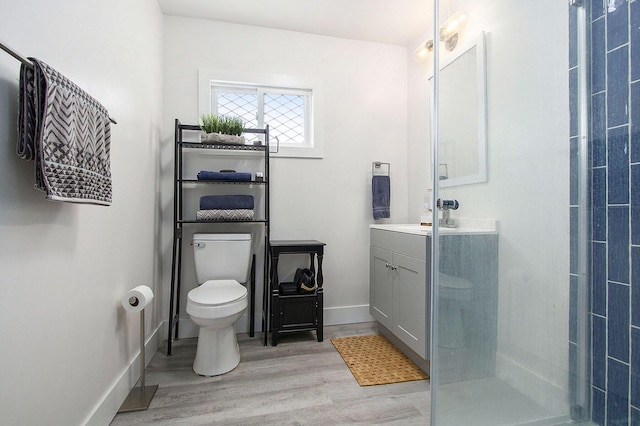 bathroom with toilet, wood finished floors, vanity, tiled shower, and baseboards