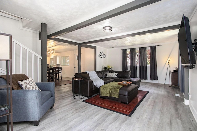 living room featuring beam ceiling, a chandelier, wood finished floors, baseboards, and stairs
