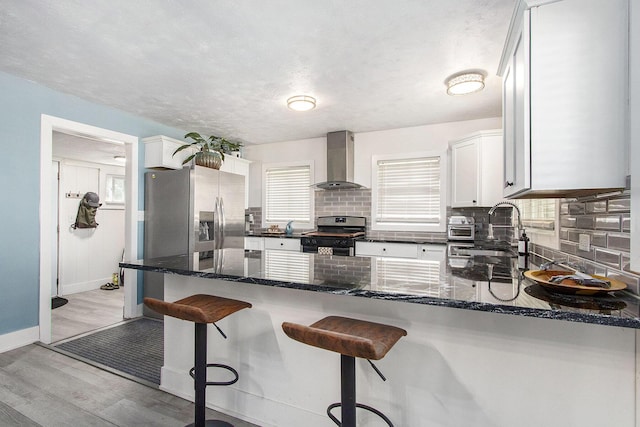 kitchen with gas range oven, wall chimney exhaust hood, a sink, stainless steel fridge with ice dispenser, and decorative backsplash