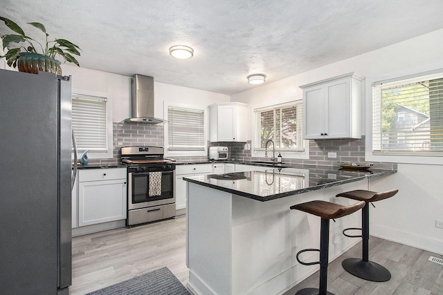 kitchen with appliances with stainless steel finishes, wall chimney range hood, a peninsula, a sink, and plenty of natural light