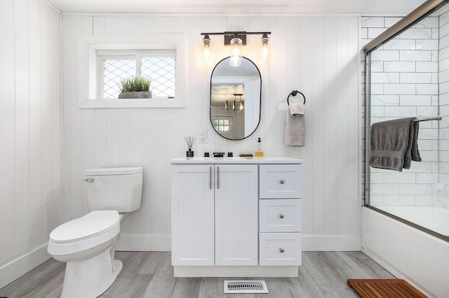 full bath featuring wood finished floors, toilet, vanity, bath / shower combo with glass door, and baseboards